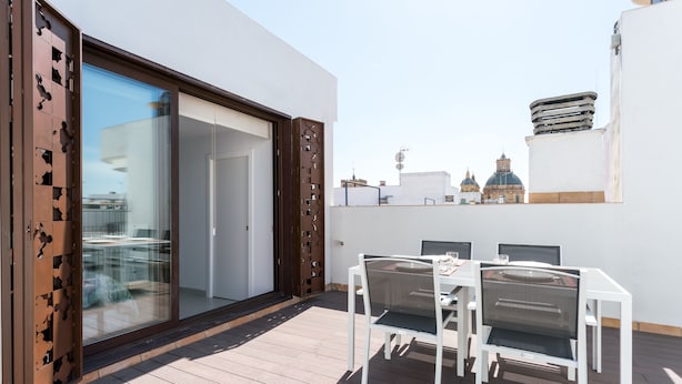 Patio esterno con tavolo e sedie, una porta scorrevole in vetro e vista su un panorama urbano con edifici a cupola.