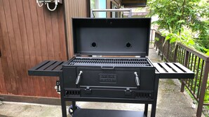 A black portable grill with wheels, a handle, and a vented lid, placed on a concrete surface. - Alps Aunty Cottage (Hakuba)