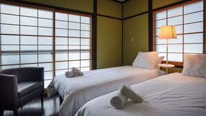 A hotel room with two beds, a chair, and a lamp. - Alps Aunty Cottage (Hakuba)