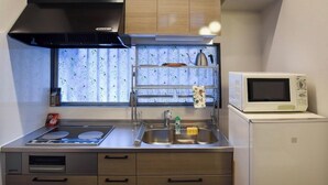 A compact kitchen with a microwave, stove, and sink. - Alps Aunty Cottage (Hakuba)