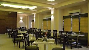 A spacious dining area with multiple tables and chairs, ceiling fans, and an air conditioning unit. - Hotel Regency (Varanasi)