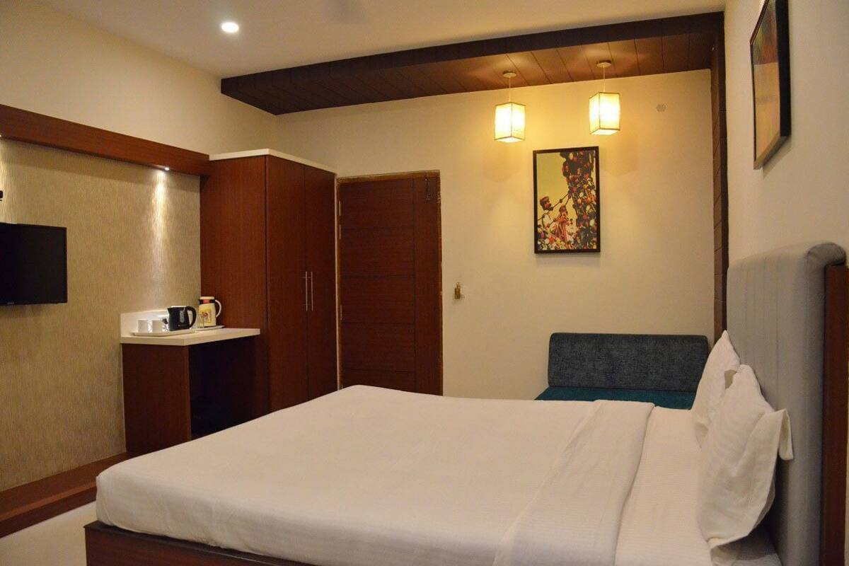 A hotel room with a bed, a wardrobe, a bedside table with a cup and a kettle, and a painting on the wall.