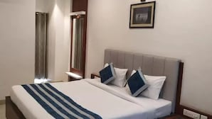 A hotel room with a bed, a nightstand, a mirror, and a framed picture on the wall. - Hotel Regency (Varanasi)