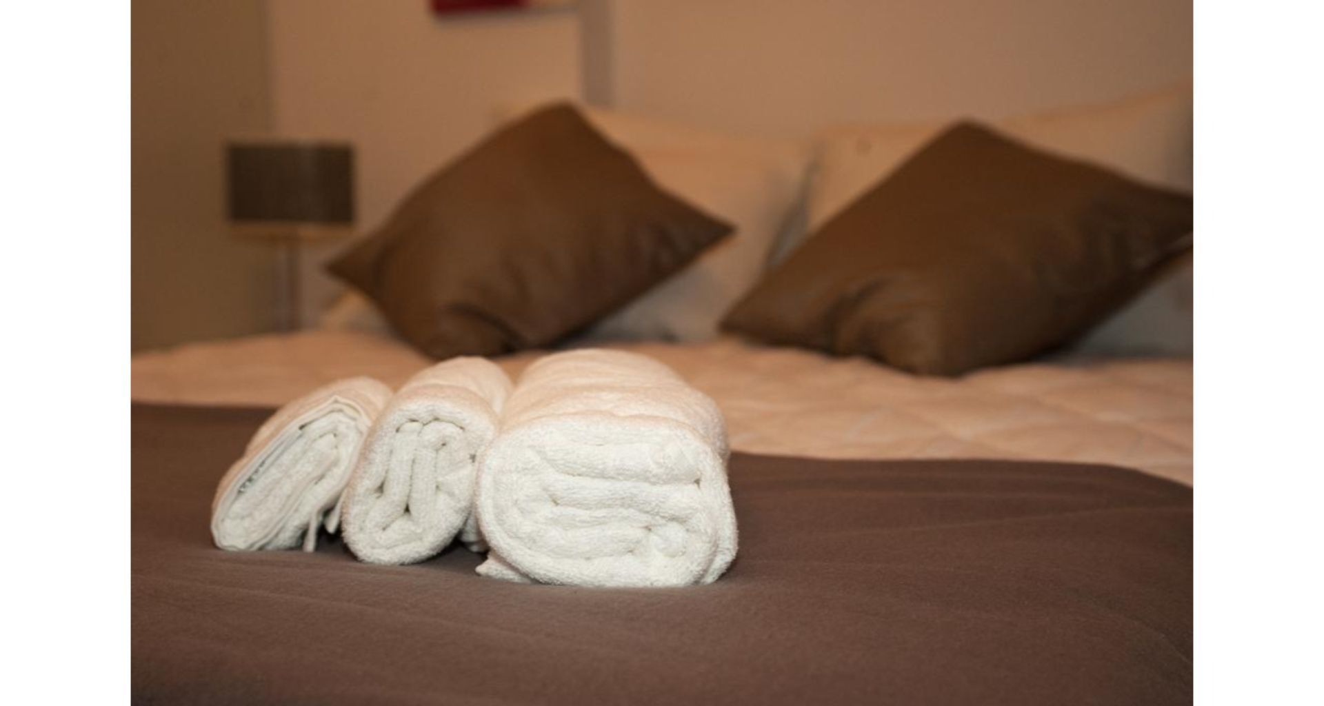 A neatly made bed with brown and white pillows and rolled white towels.