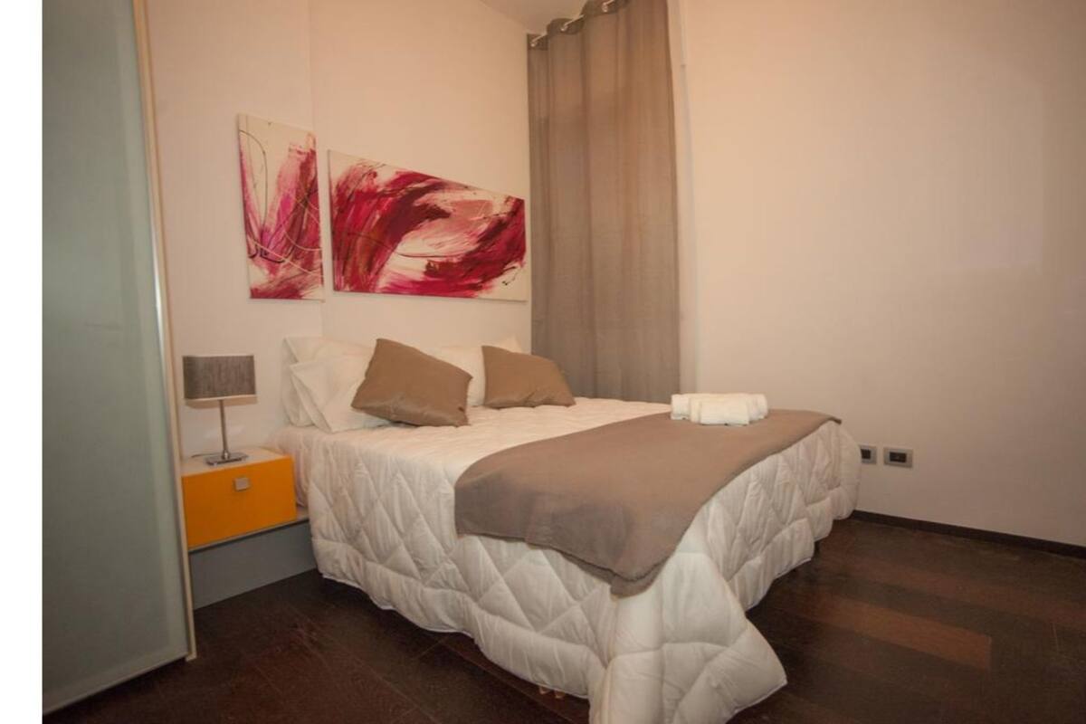 A bedroom with a bed, pillows, a blanket, a nightstand, and abstract wall art.