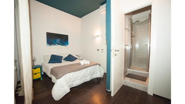 A bedroom with a bed, a bedside table, a wall-mounted artwork, and a shower area. - Da Molly (Rome)