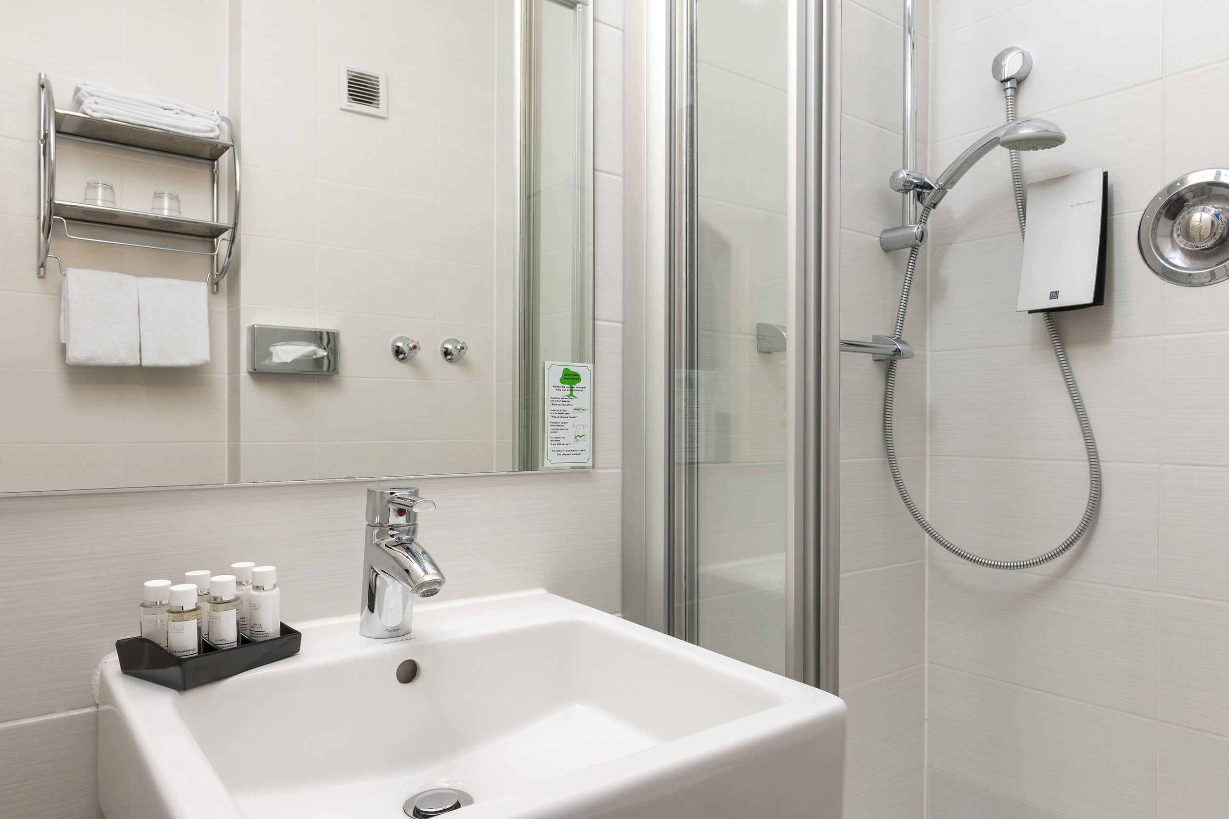 A bathroom with a white sink, a glass shower enclosure, and a towel rack with folded towels.