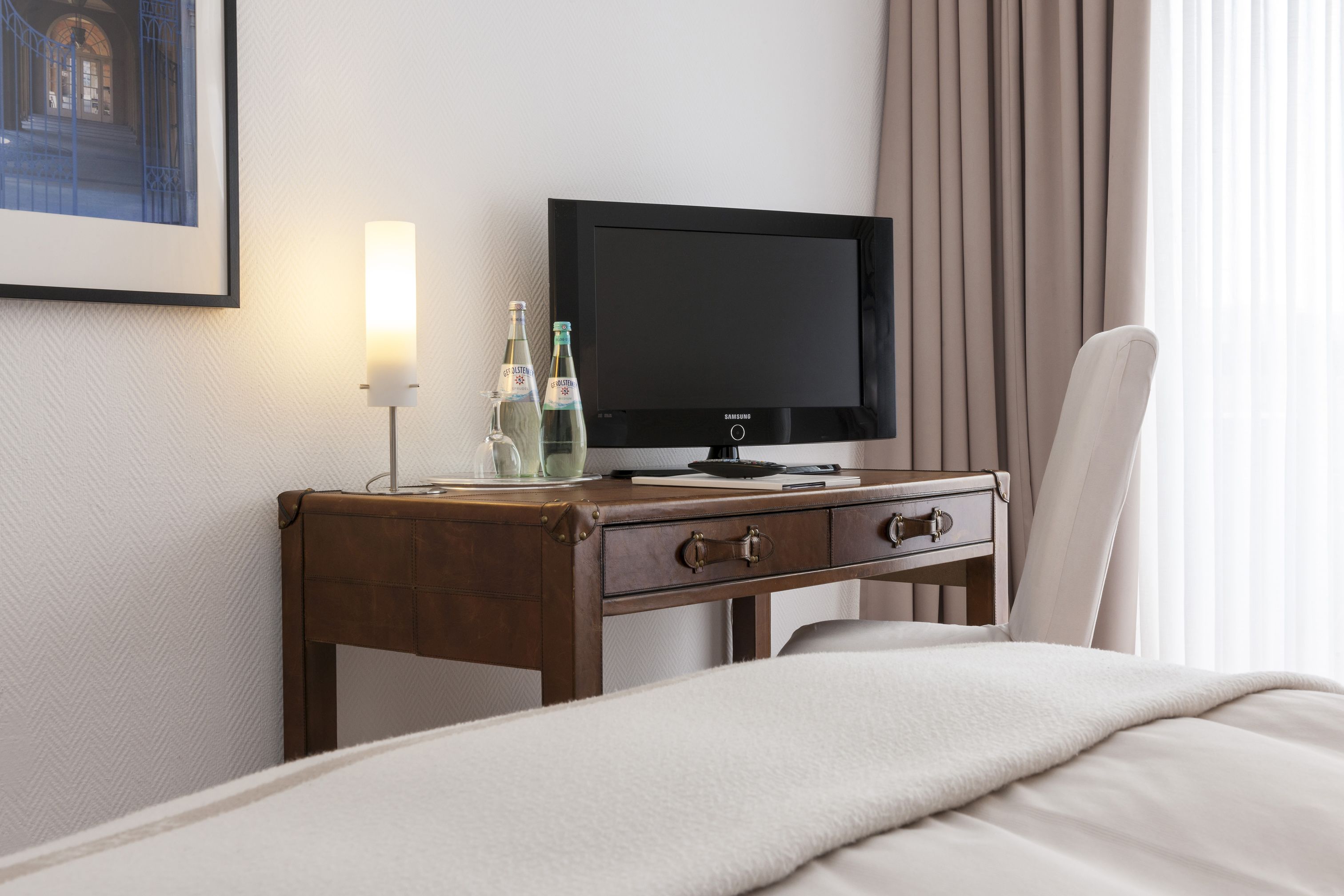 Een hotelkamer met een bed, een houten nachtkastje met een televisie, een lamp en twee waterflessen.