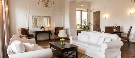 Un salón amplio y elegantemente amoblado con un sofá blanco, un sillón a juego, una mesa de centro y una araña.