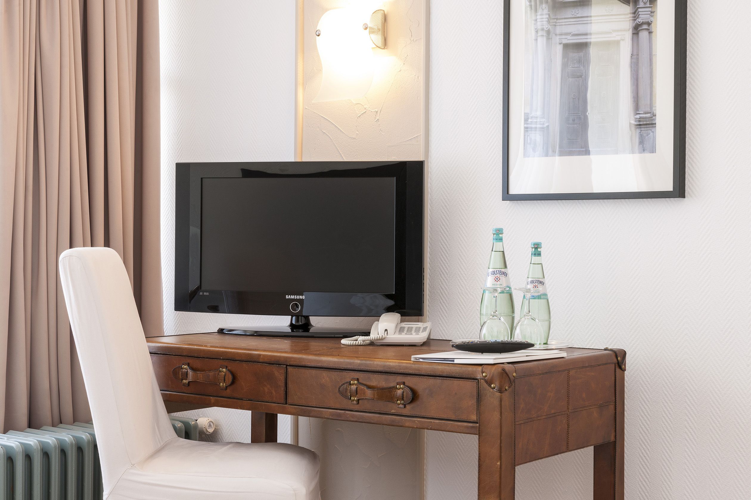 Een hotelkamer met een houten bureau, een televisie, een telefoon en twee flessen water.
