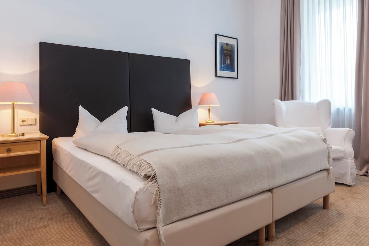 Een hotelkamer met een groot bed, twee nachtkastjes, een stoel en een raam met gordijnen.