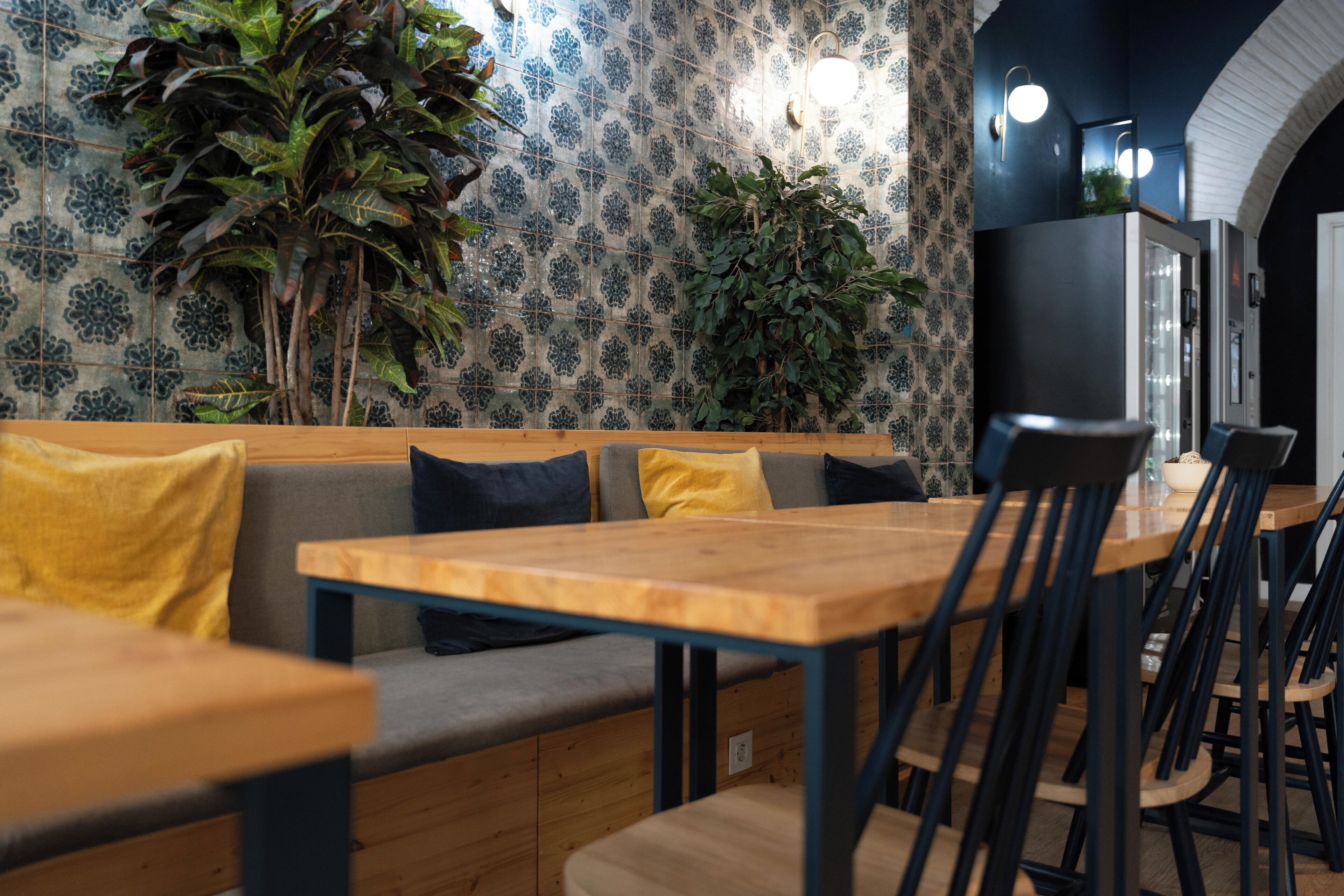 Een restaurantinterieur met houten tafels en banken, betegelde muren met een patroon en groene planten.