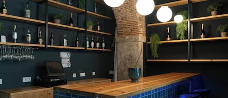A bar area with wooden shelves holding bottles and glasses, a wooden counter, and blue-tiled backsplash.