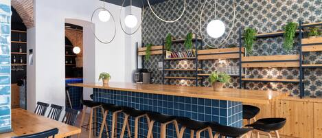 Zona de bar moderna con barra de madera, taburetes negros y un revestimiento de pared con diseño.