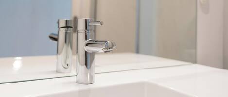 A modern bathroom with a white sink, chrome faucet, and a glass shower enclosure.