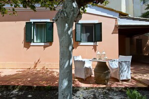 Une terrasse avec une table dressée pour deux personnes, un grand vase et un arbre au premier plan.