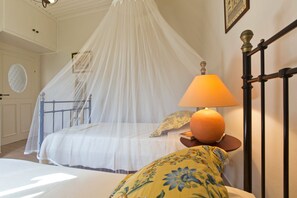 Une chambre à coucher avec un lit sous un dais, une table de chevet avec une lampe et un coussin à motifs floraux.