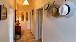 A hallway with a wooden floor, a hanging lamp, and a wall-mounted hat rack with several hats. - Casa Paleopolis near Royal Baths MonRepo (Corfu)