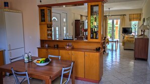 A kitchen with a wooden island, dining table, and chairs. There is a refrigerator, cabinets, and a television in the background. - Hidden gem in nature reserve on the beach (Corfu)