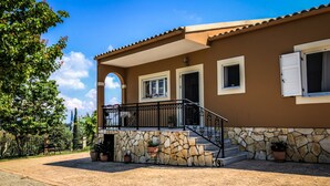 A two-story house with a stone facade, a balcony with a metal railing, and a paved driveway. - Hidden gem in nature reserve on the beach (Corfu)