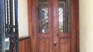 A wooden double door with a metal gate on the left, leading to a checkered floor. - Tas Suite Konukevi (Gökçeada)