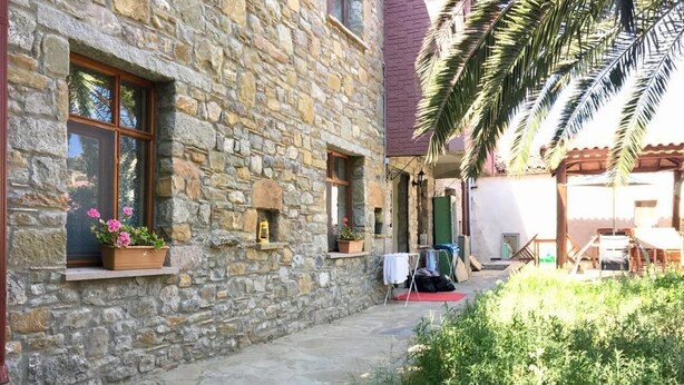 A stone building with a courtyard, a wooden pergola, and potted plants. - Tas Suite Konukevi (Gökçeada)