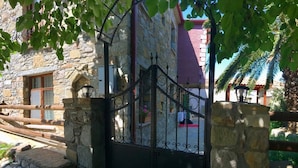 A stone building with a wrought iron gate, a red roof, and a view of a courtyard with a palm tree. - Tas Suite Konukevi (Gökçeada)