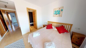 Ein Schlafzimmer mit einem Bett, zwei roten Kissen, einem hölzernen Kopfteil, einem Nachttisch, einem Wandbild und einem durchgehenden Durchgang zum Badezimmer.