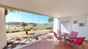 Ein Balkon mit Seeblick, eine Essecke mit roten Stühlen und eine Tür mit Fenster.