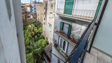 A multi-story building with balconies, a view of the surrounding neighborhood, and a lush green area below.