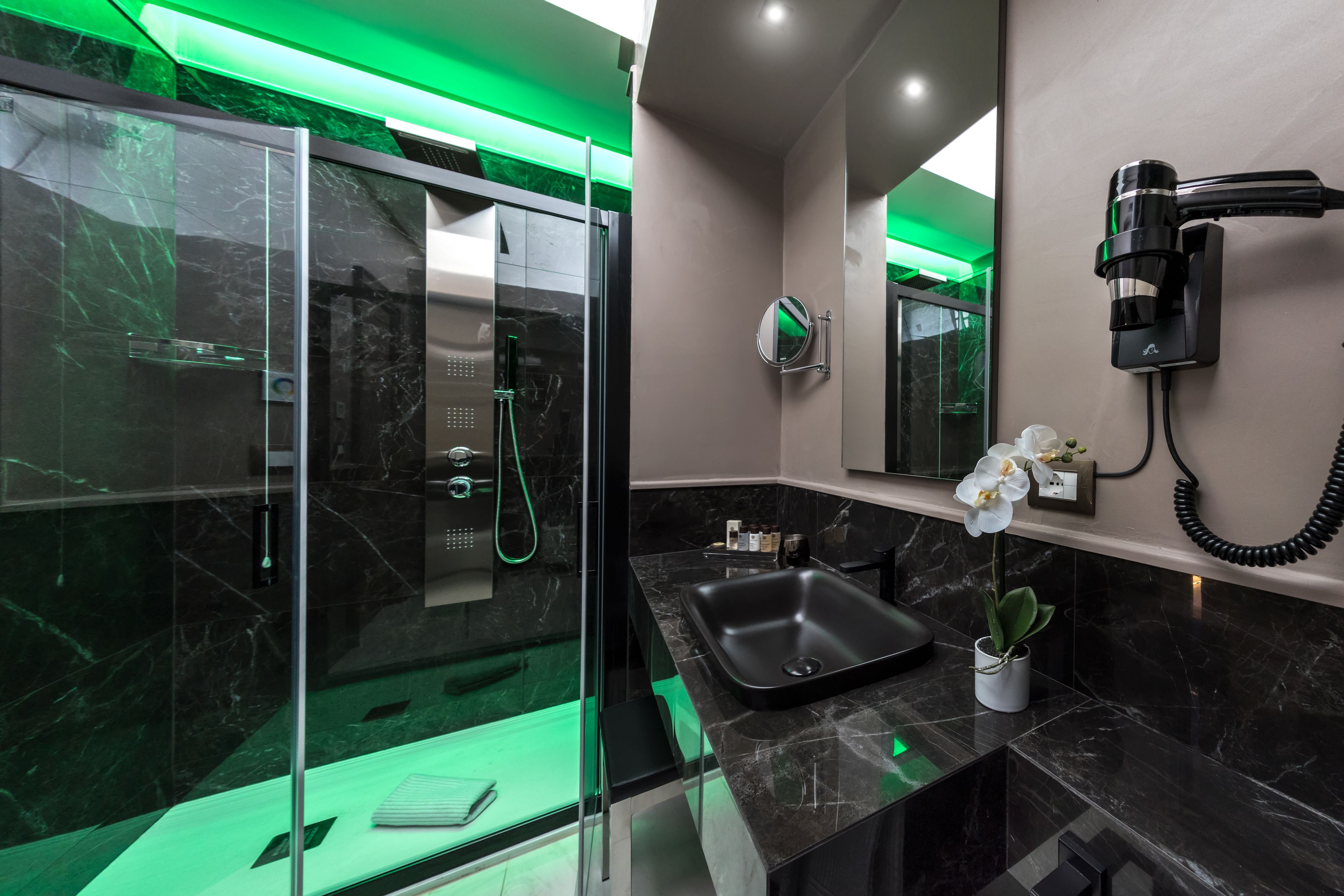 A modern bathroom with a glass-enclosed shower, a black sink, and a hairdryer mounted on the wall.