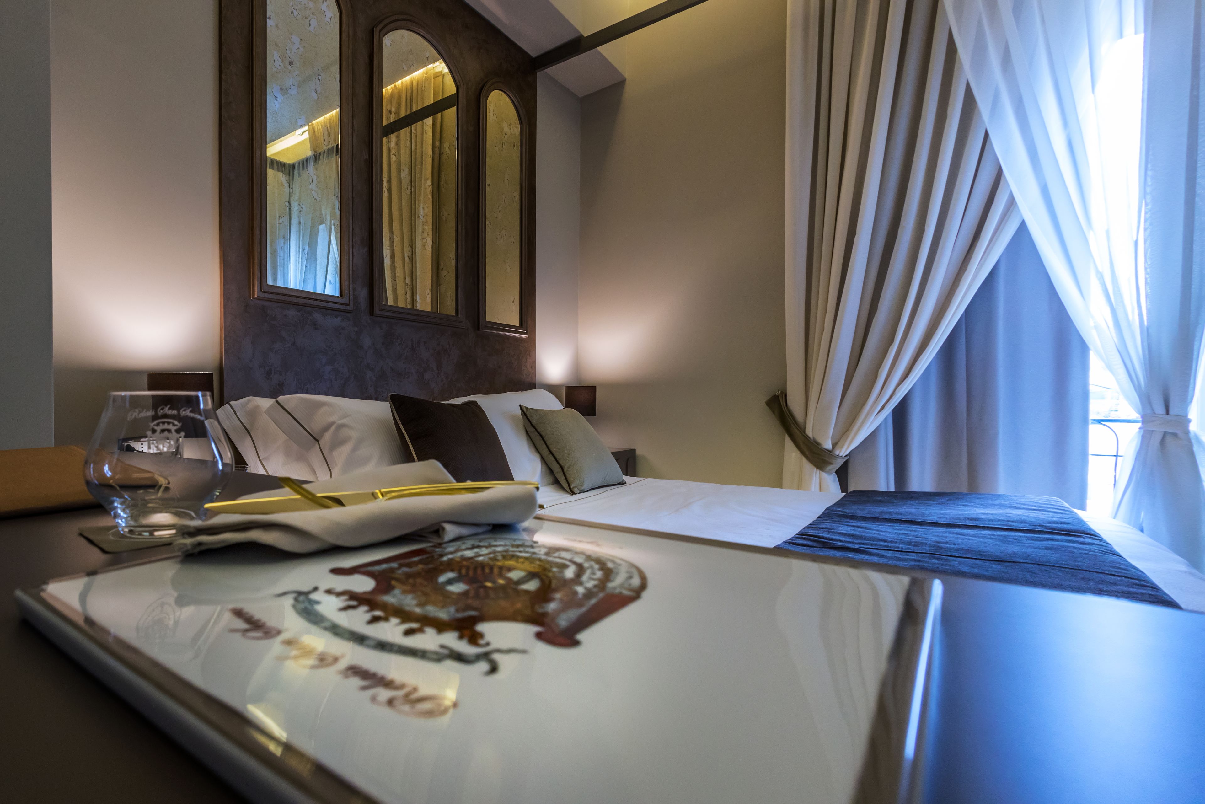 A hotel room with a neatly made bed, a bedside table with a glass, and a framed picture.