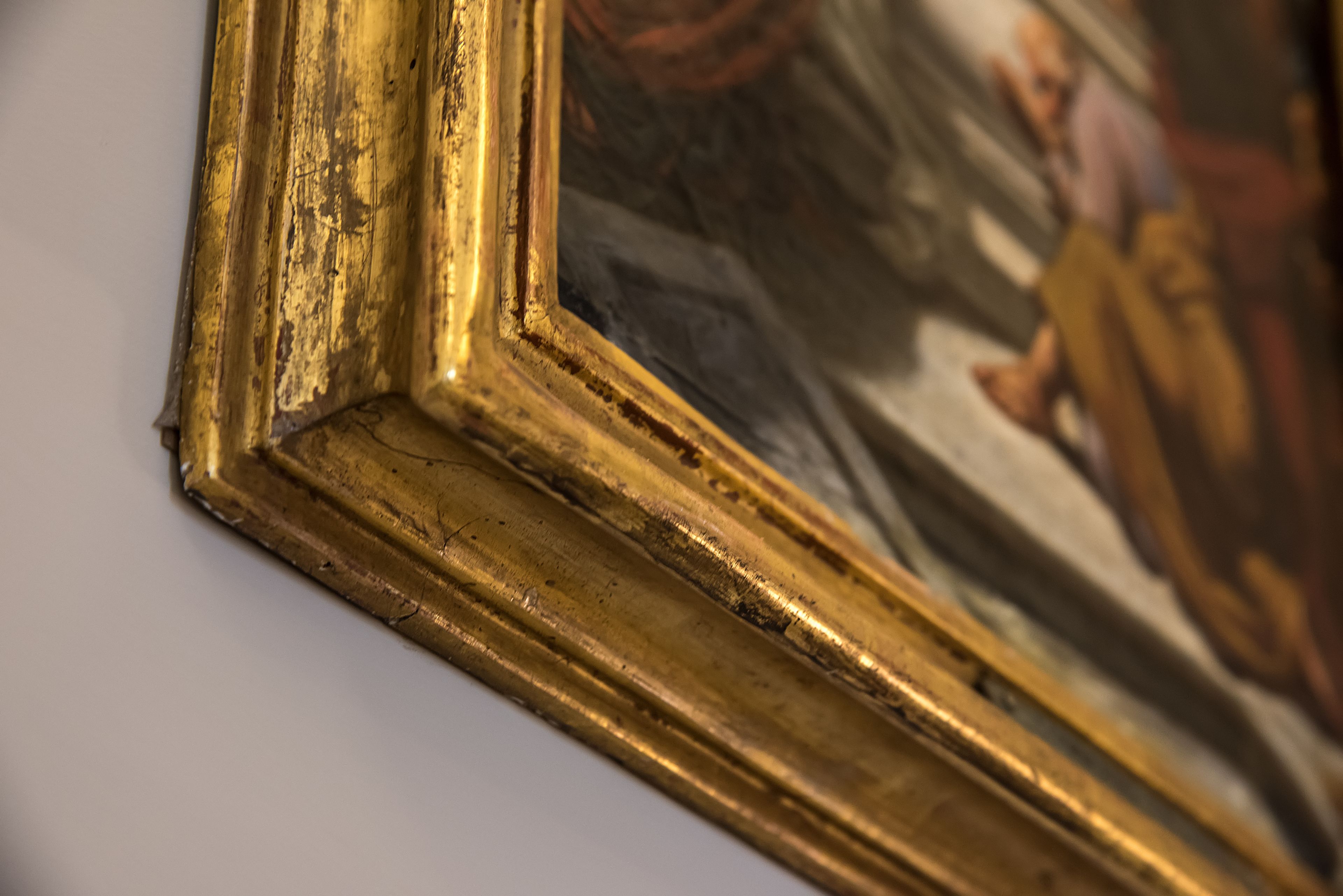 Un gros plan d’un tableau encadré d’un cadre doré, sur lequel on peut voir des signes d’usure et d’altération.