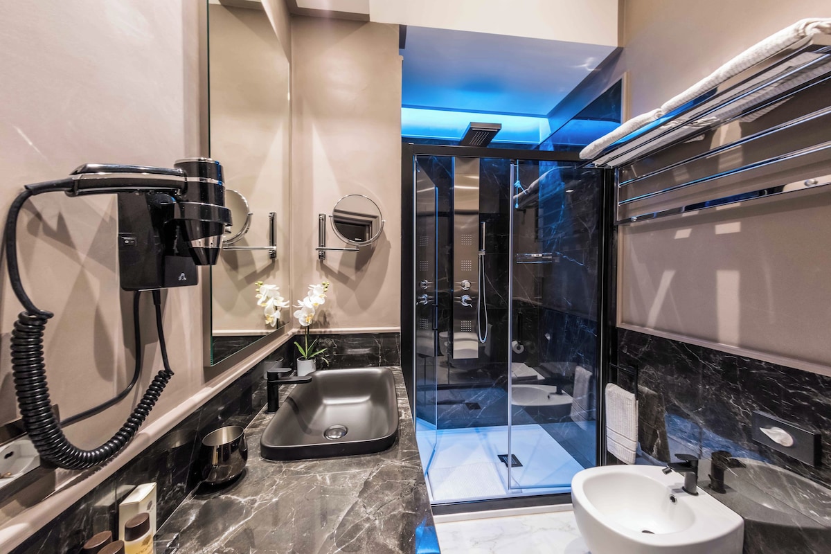 A modern bathroom with a glass-enclosed shower, a sink, and a hairdryer mounted on the wall.