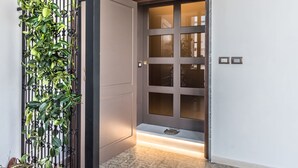 Una entrada moderna con una puerta oscura, una reja metálica con follaje y un escalón iluminado.