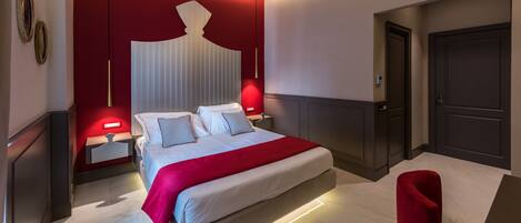 A modern hotel room with a large bed, red accent walls, and a red chair.