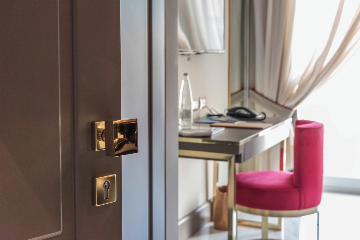 Habitación de hotel con una puerta, un escritorio, una silla y un espejo.