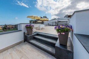 A rooftop terrace with outdoor seating, potted plants, and a view of the city.