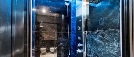 A modern bathroom with a glass-enclosed shower, marble walls, and a visible toilet area.