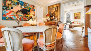 Un coin repas avec une table en marbre et des chaises d’époque, une grande peinture abstraite et un portrait classique.