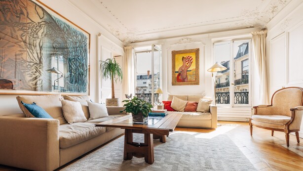 Un salon spacieux avec un canapé beige, une table basse en bois et un grand tableau accroché au mur.