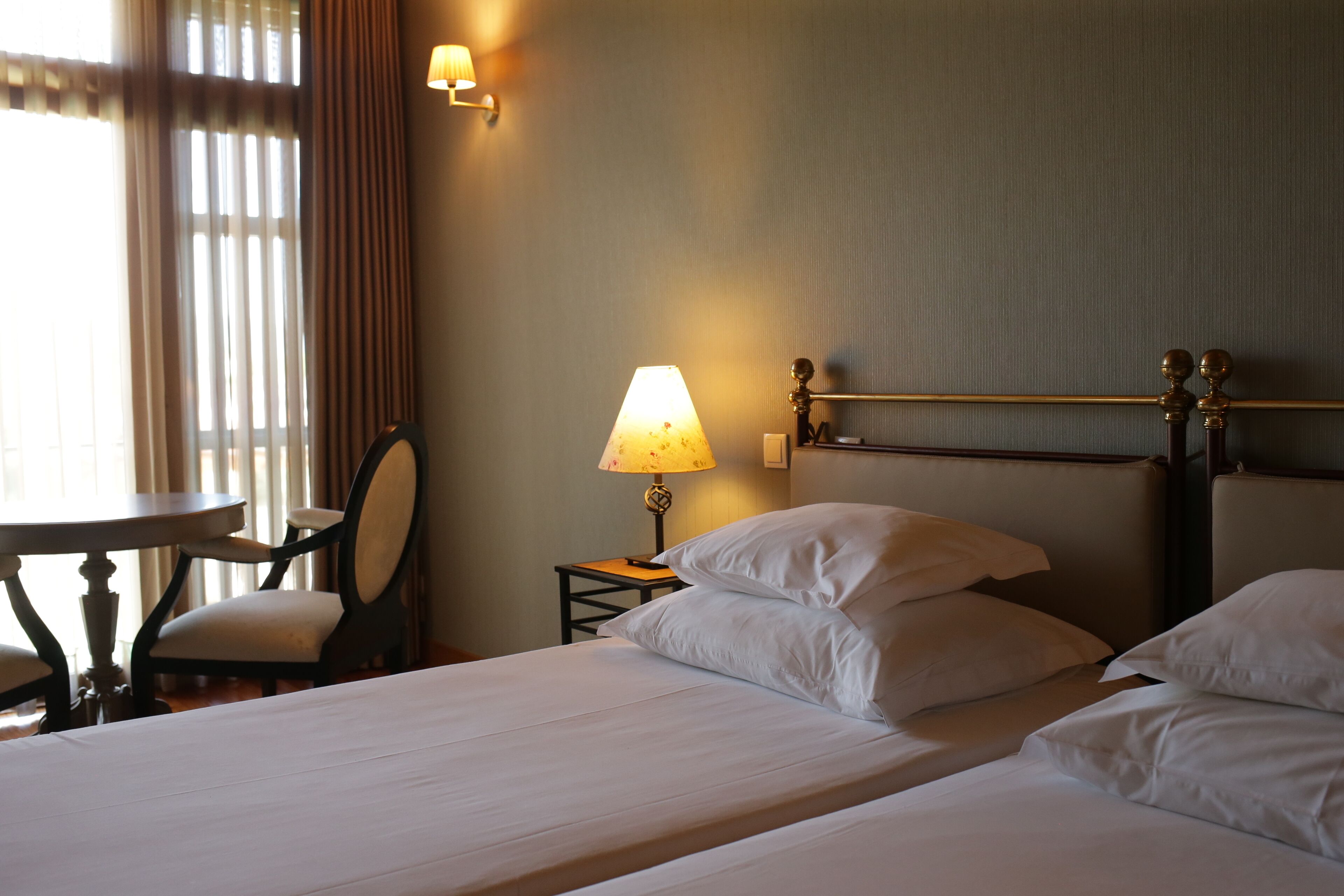 A hotel room with a bed, a bedside table with a lamp, a chair, and a window with curtains.