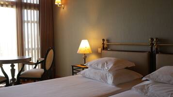 A hotel room with a bed, a bedside table with a lamp, a chair, and a window with curtains.