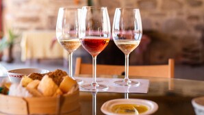 Una mesa de comedor con tres copas de vino, una cesta de pan y un plato de queso.