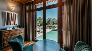 Una habitación con piso de madera, una mesa redonda, dos sillas tapizadas en verde, un aparador de madera, un espejo y vista a una piscina exterior a través de puertas de vidrio amplias.