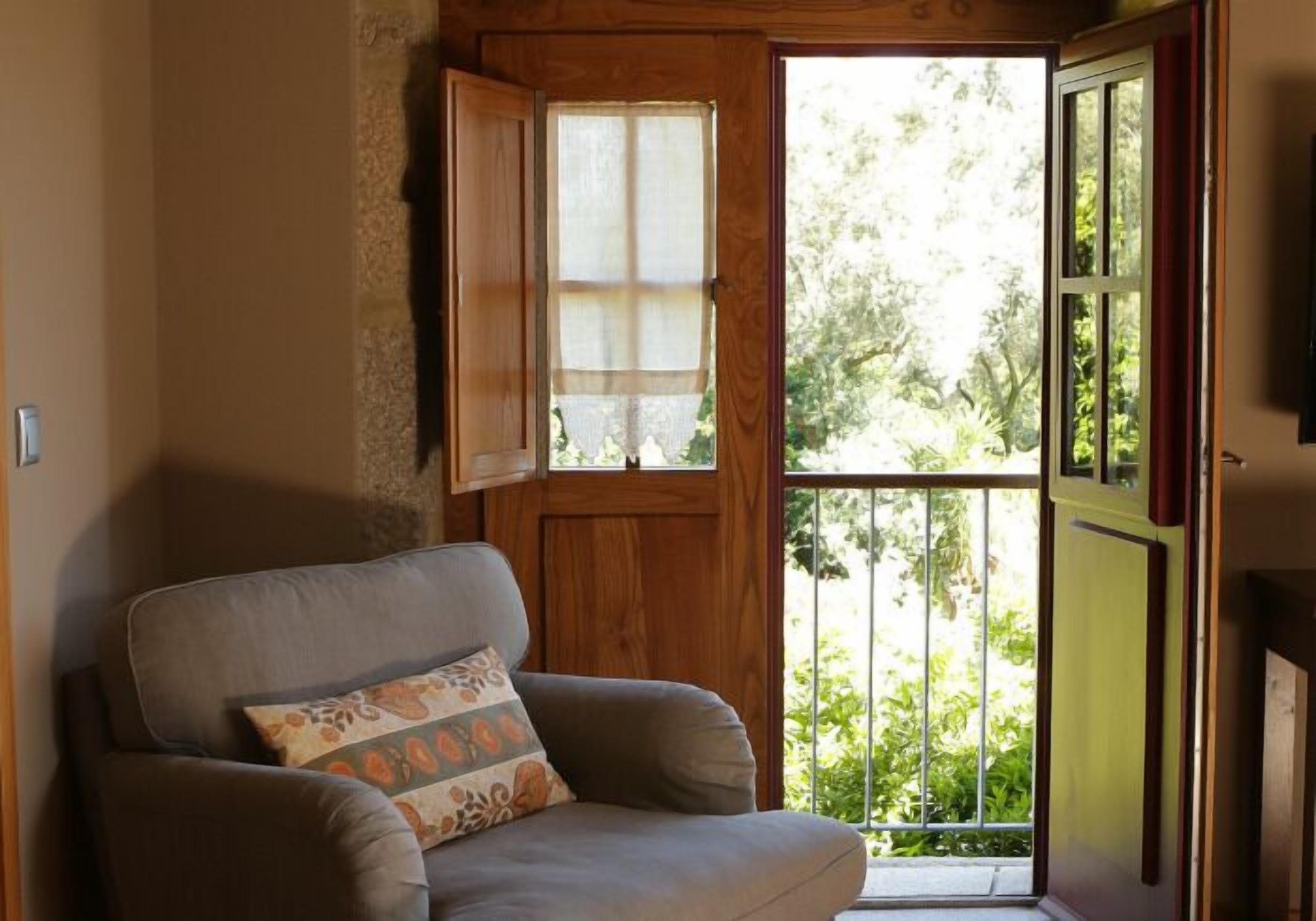 A cozy room with a wooden door, a cushioned armchair, and a view of greenery outside.