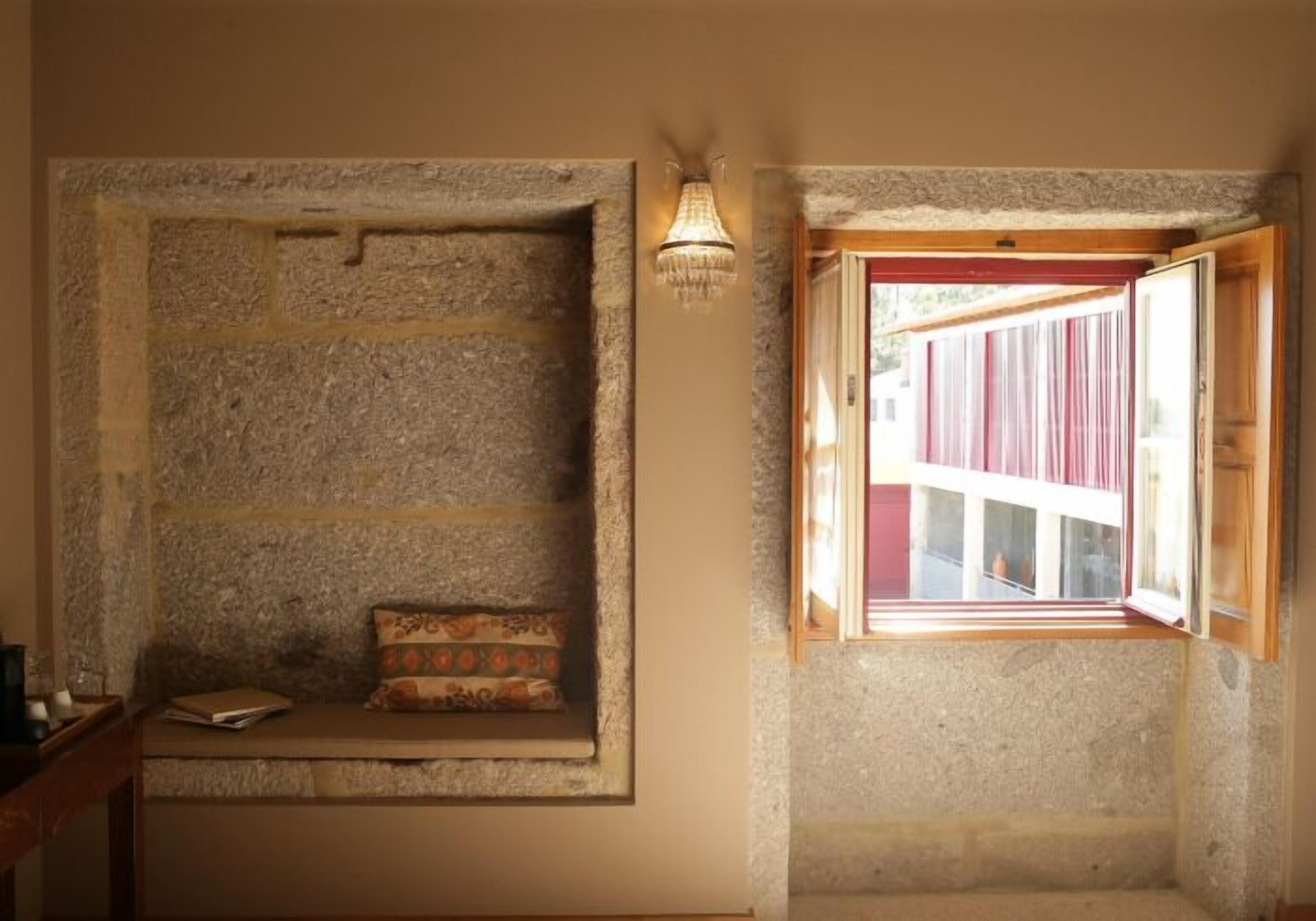 A stone bench with a cushion, a small table, and a window with red curtains.