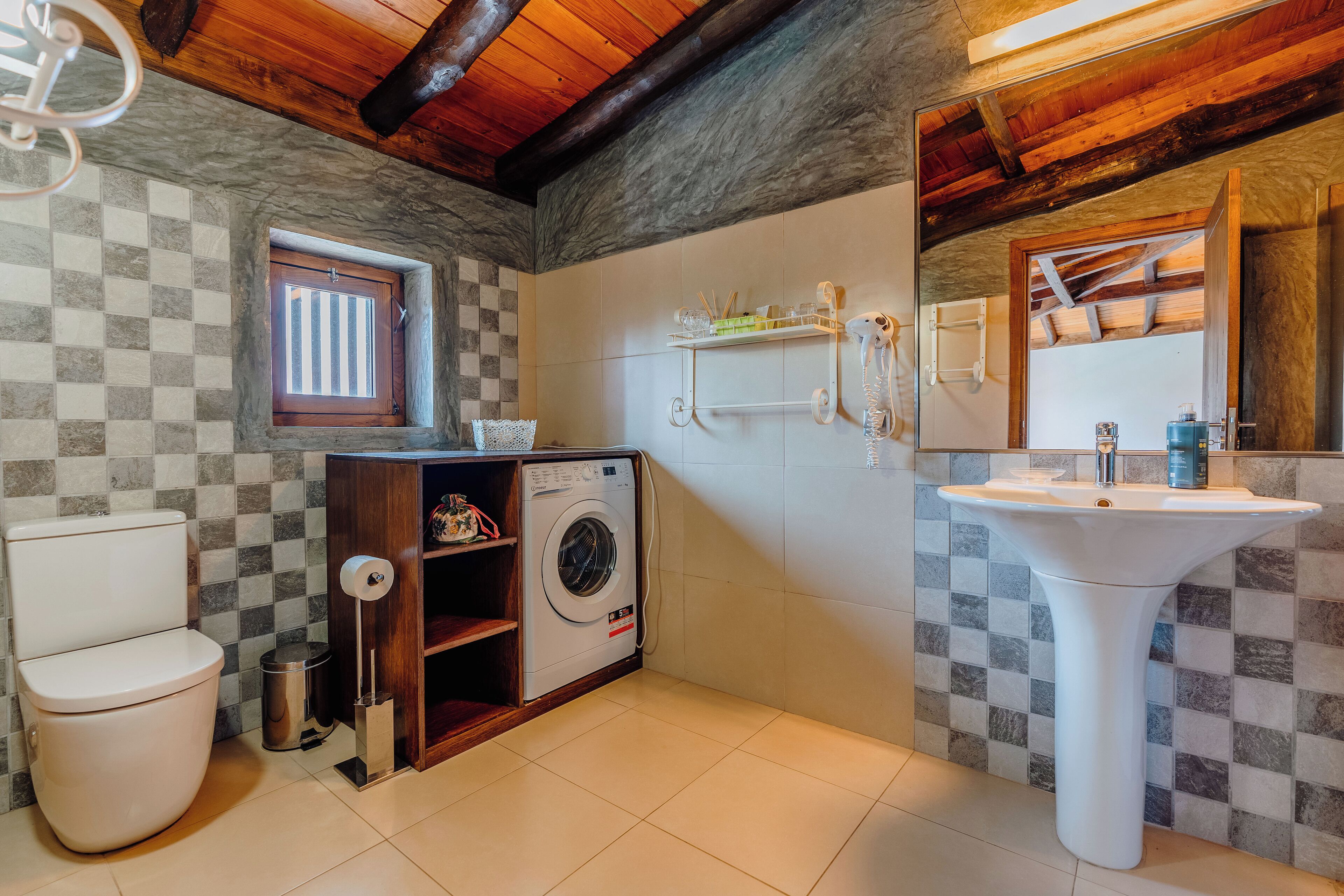 Un baño con lavadora, inodoro, lavabo y ventana con pared a cuadros.