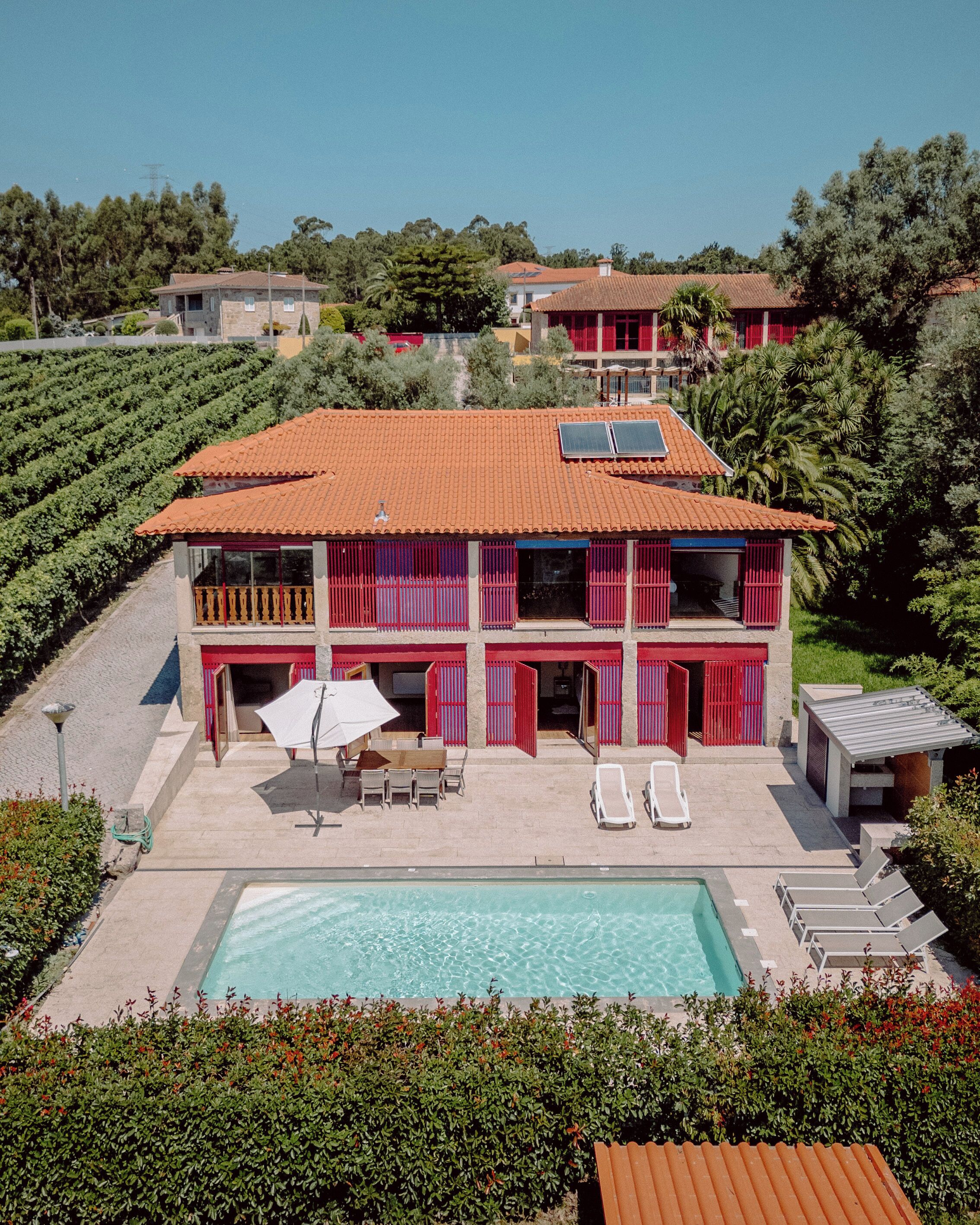 A two-story building with a red-tiled roof, a swimming pool, and a patio area with lounge chairs and a table.