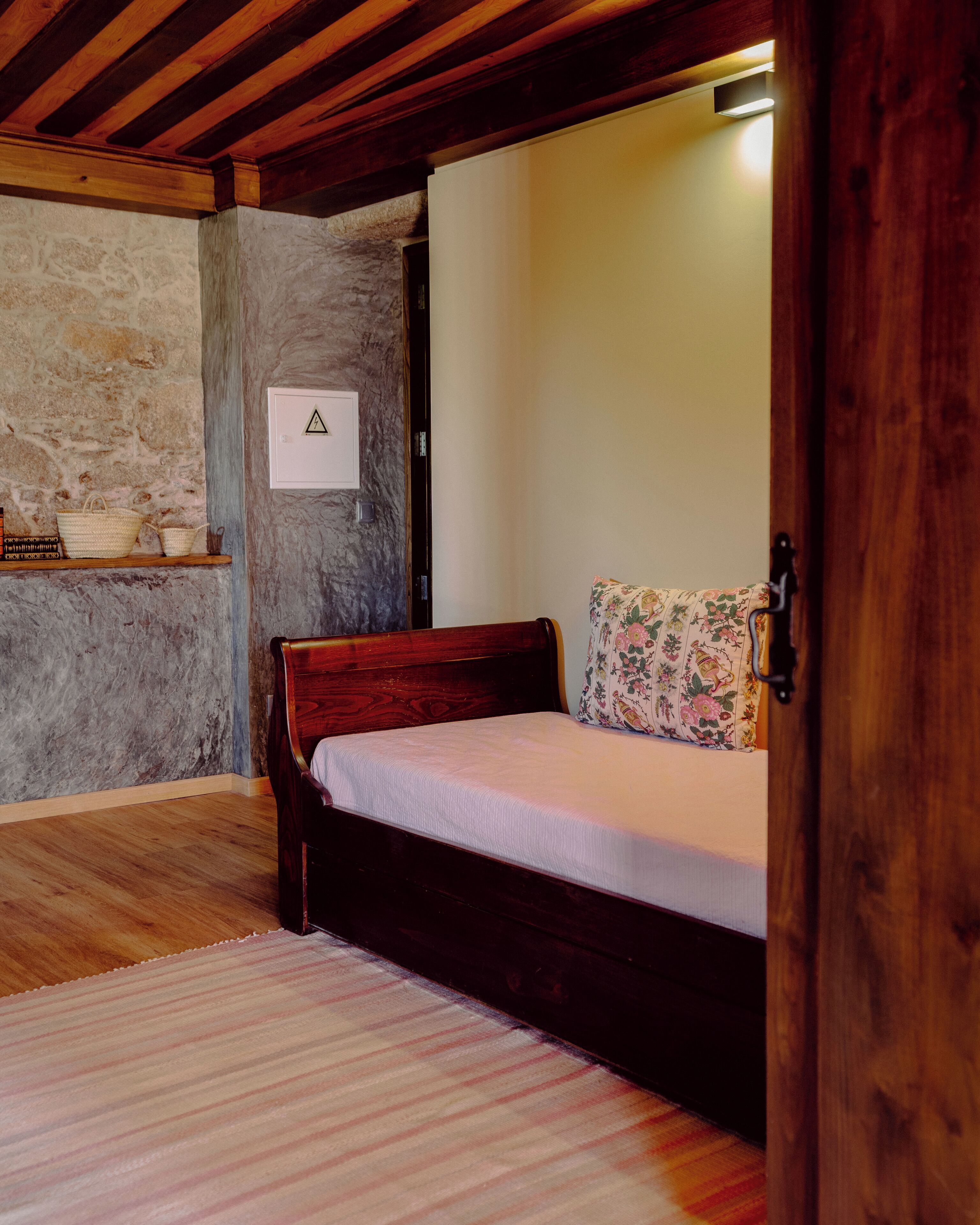 A bedroom with a wooden bed, a stone wall, and a small shelf with baskets.